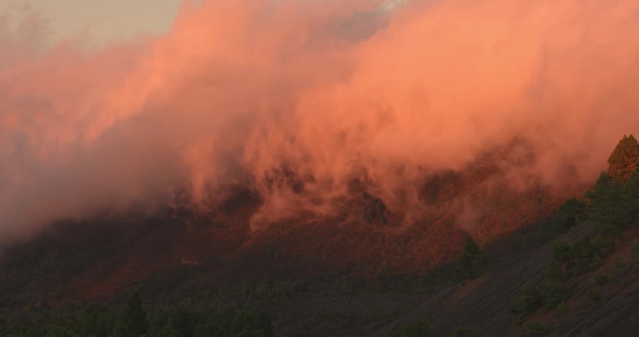 A massive bank of clouds pours down the side of a mountain at dusk