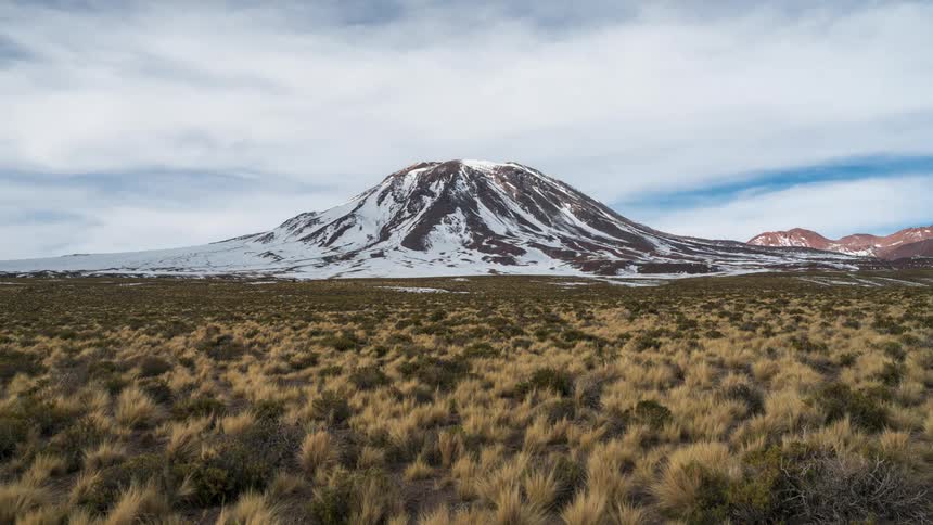 Clouds pass over snowy mountain towering over scrub land during winter