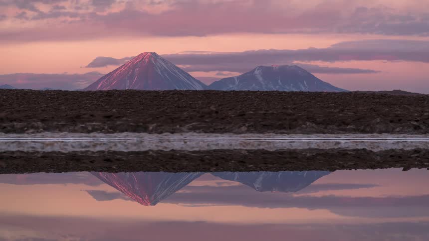 Lake reflecting snowy mountains on the horizon against a partly cloudy sky