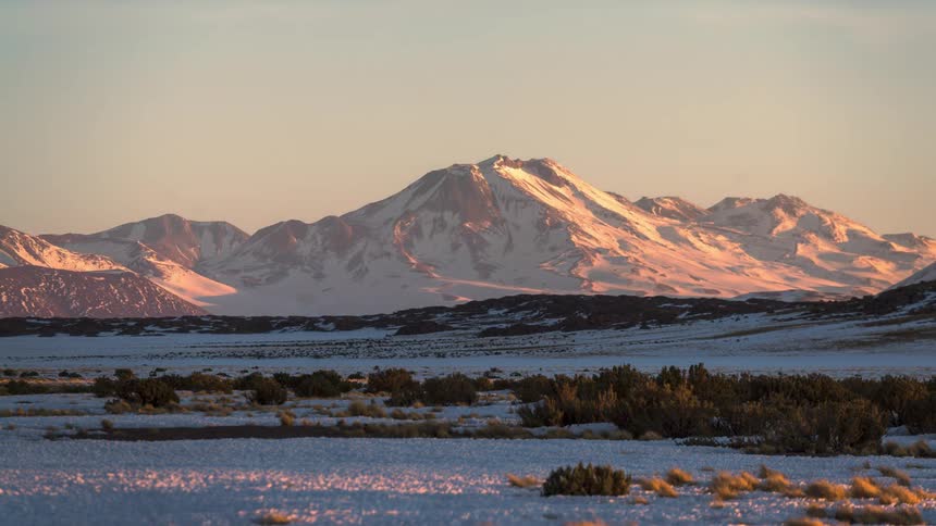 Mountainous landscape covered in snow with the sky turning red in the late afternoon