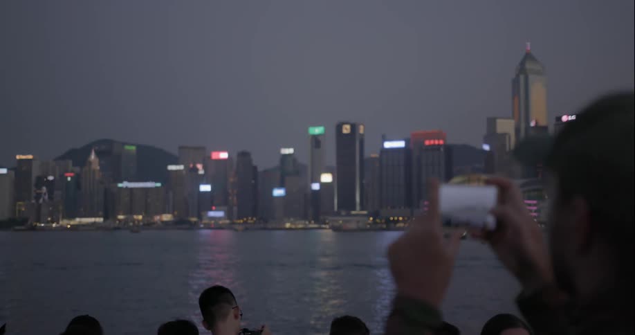 A man uses his cellphone to take a picture of a city skyline at dusk