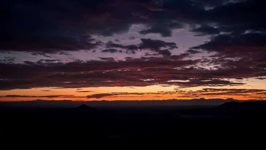 Landscape of mountain silhouettes against a cloudy sky with a reddish color on the horizon