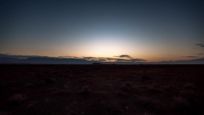 The sun rises over sparse tumbleweeds in a desert