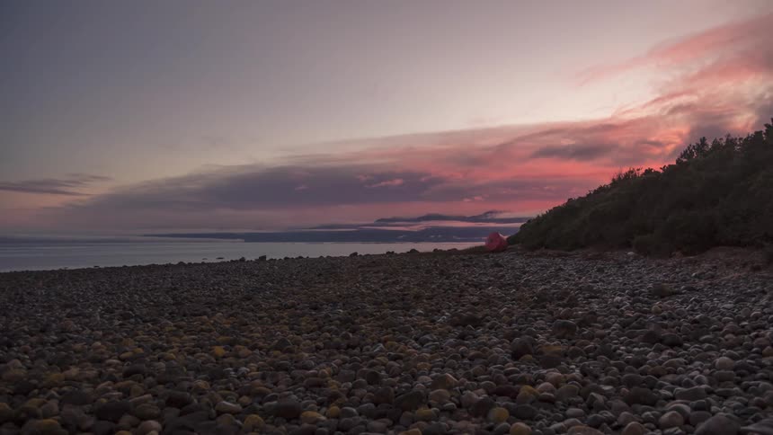 Time lapse of clouds rolling over a beach covered in pebbles at sunrise