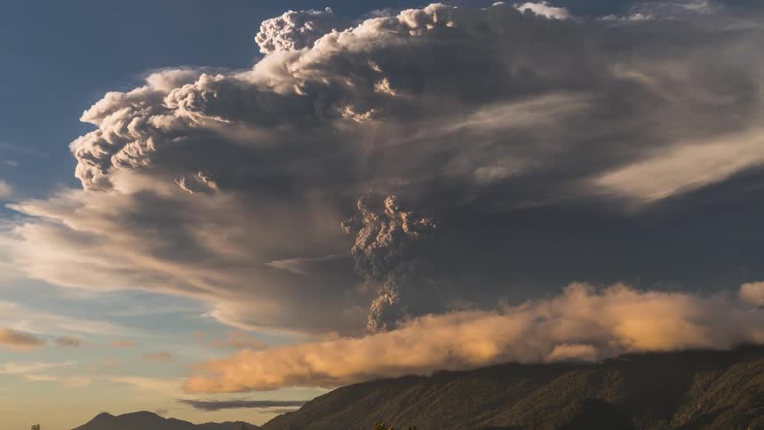 Small clouds flow under one large cloud over the mountains by a lake