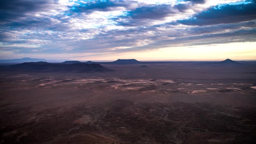 Vast desert landscape under a clear blue sky that darkens with overcast clouds