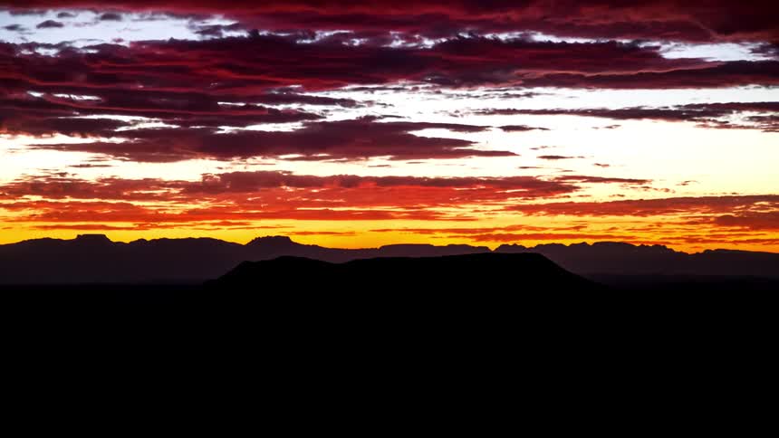 Time lapse of clouds rolling over a colorful golden sky at sunset over a dark landscape