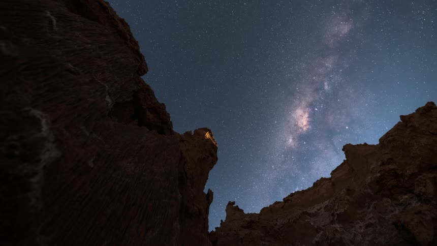 View of the sun setting and the sky becoming starry with the milky way visible between two large rock formations