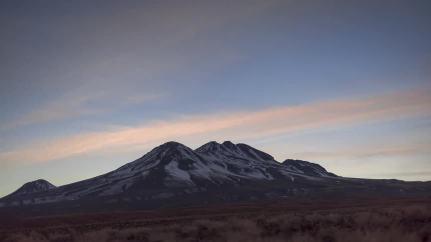Night sky with stars changing to shades of pink and dawn above snowy mountains