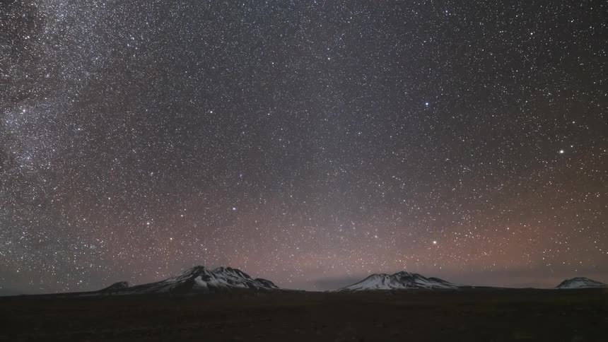 Landscape of a rocky terrain with snowcapped mountains on the horizon and a twilight sky showing the milky way