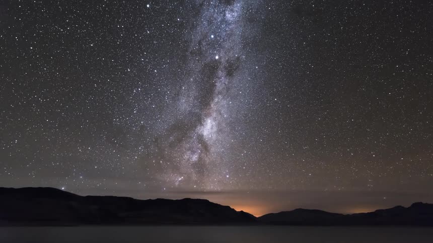 Silhouette landscape of mountains by a lake with a stellar night sky