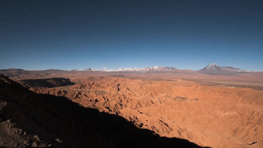 Landscape of rocks and mountains on the horizon with snowcapped peaks against a blue dusk and dawn sky