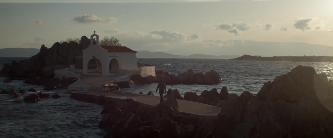 Person walking towards a house by the water on a cloudy day