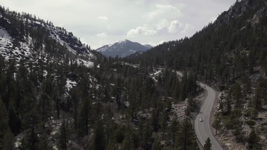 Highway running through forest and mountains partially covered in snow