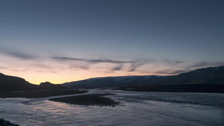 A time lapse shows a river flowing swiftly as the sun has set in the sky