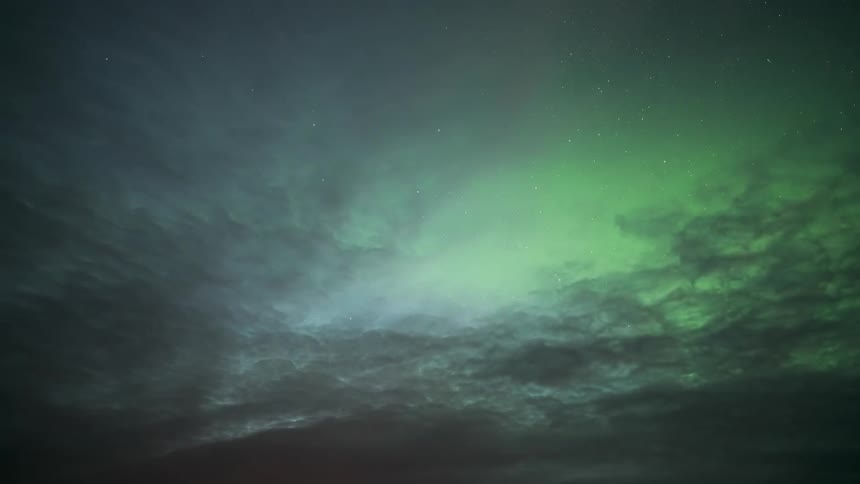 Moving clouds partially obscure the aurora borealis in the starry night sky
