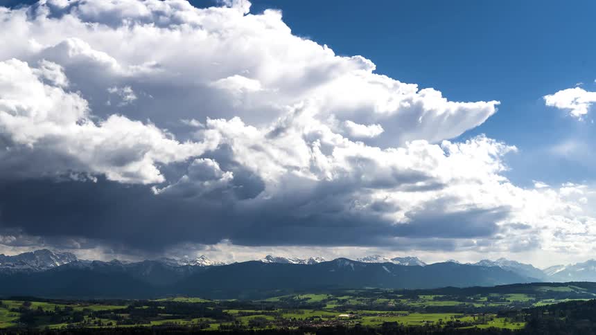 Time lapse of clouds rolling over a mountainous landscape with green fields under a blue sky