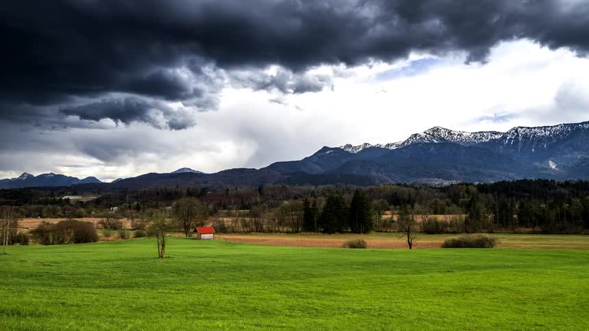 A vibrant green field stretches out under a dramatic sky with dark clouds