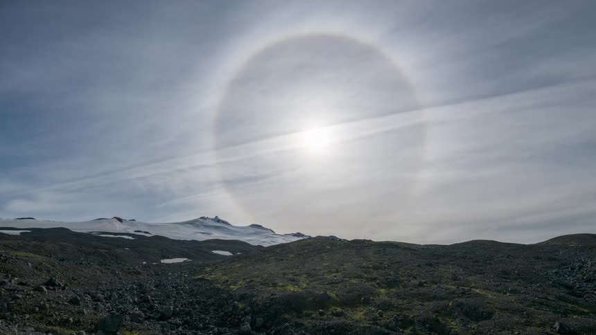The sun shines over snowcapped mountains and bare black desert