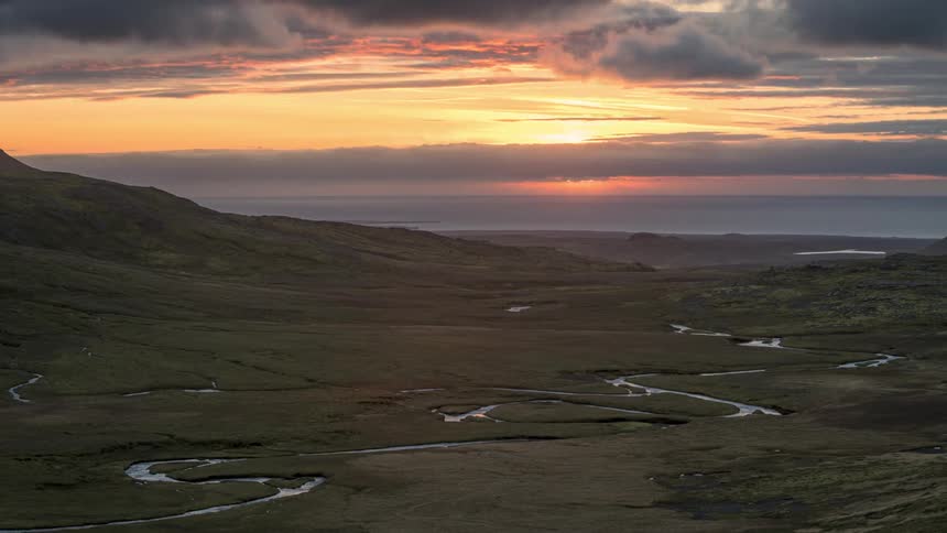 Scenery of a red sky with the sun setting on the horizon above mountains and a meandering river