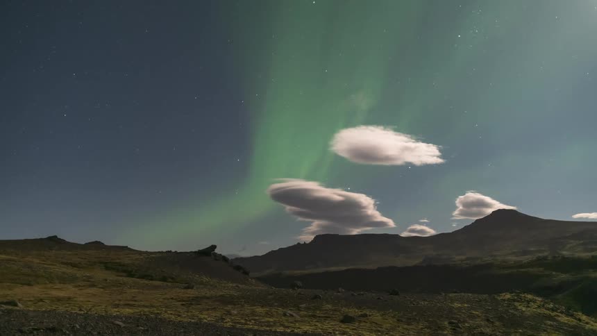 Greenish mountain scenery with northern lights passing by