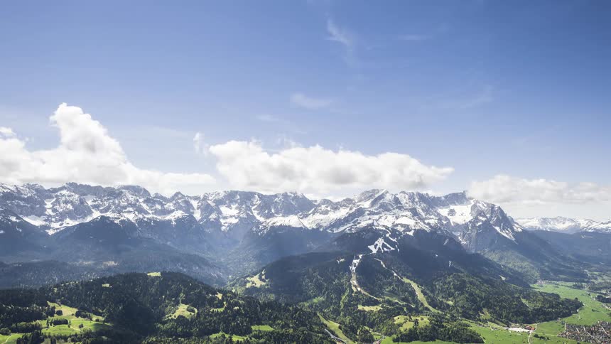 Vast snowcapped mountain range with green valleys and forests below