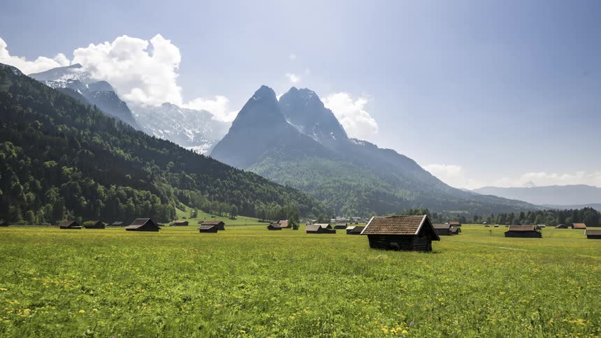 Green field with cabins surrounded by mountains with vegetation