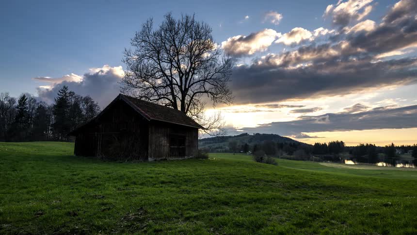 Log cabin in a grassy pasture against a darkening sky