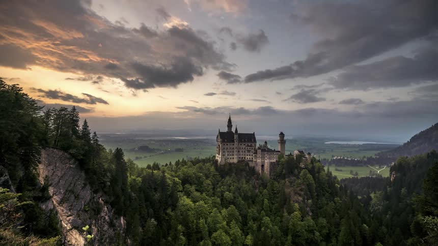 Landscape of a castle on top of a mountain surrounded by conifers against a cloudy sky