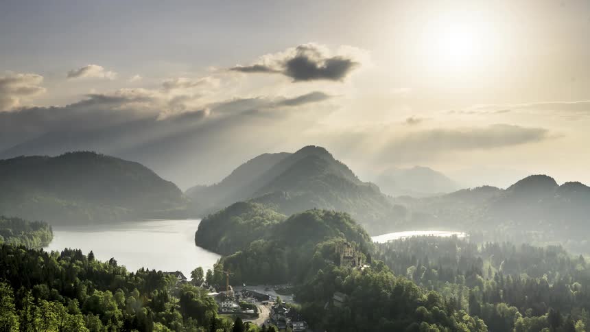 Sunlight piercing through the clouds over a serene mountainous landscape with lakes and villages