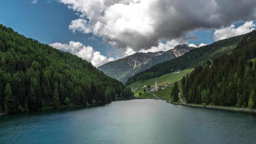 Landscape of dense clouds above mountains with conifers and on the edge of a lake