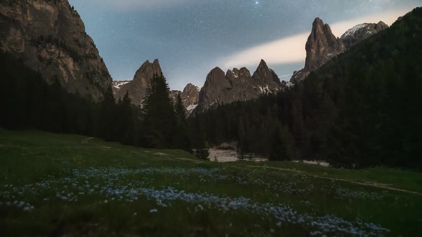 Countryside surrounded by mountains with snowcapped peaks and dense clouds passing by as the day gets dark