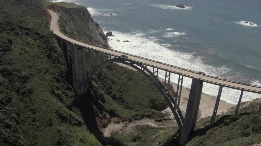 Aerial view of a long bridge spanning between high hills before the sea
