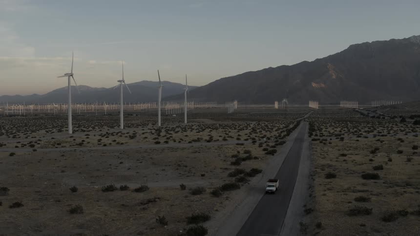 A vehicle is driving down a road past a wind-farm