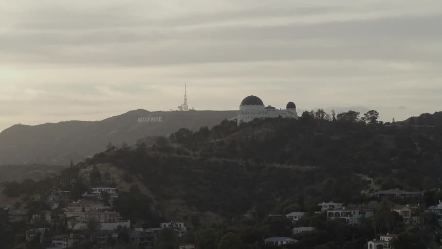 A domed building sits on the top of a hill with the hollywood sign in the background