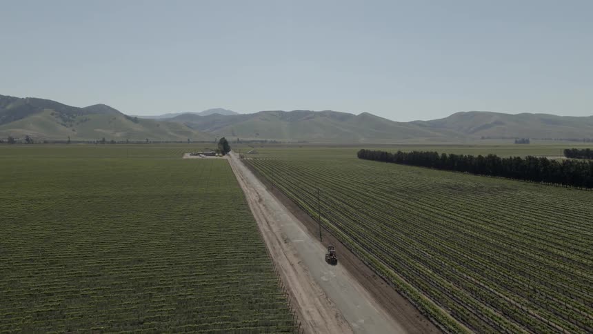 A piece of farm equipment goes down the road between two fields