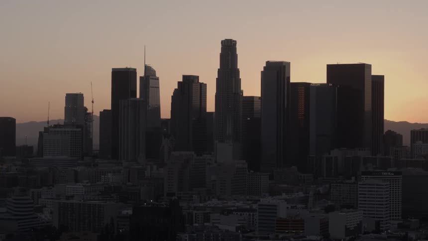 A city with tall buildings is dark as the sun sets
