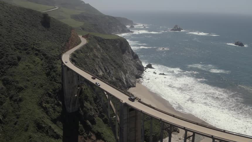 Cars driving over a tall bridge near the ocean