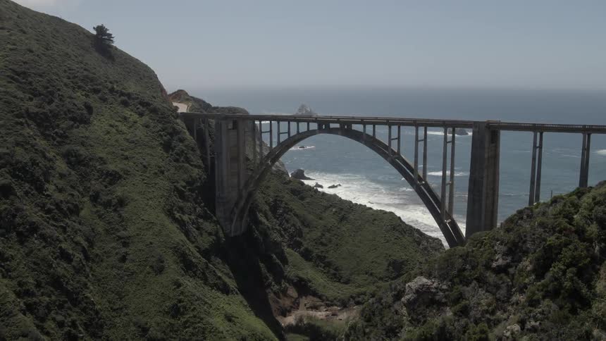 Aerial view of a long bridge spanning between high hills before the sea