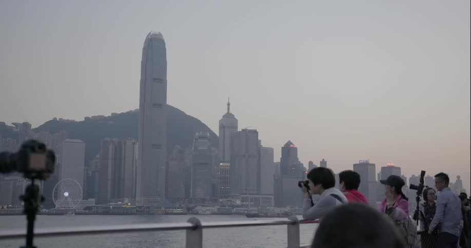 People observing and photographing large city across a bay