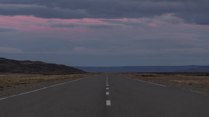 The sun is setting in the horizon of the rural road