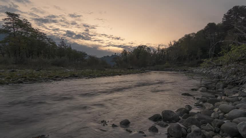 Time lapse of clouds rolling over a serene river flowing through a rocky bed