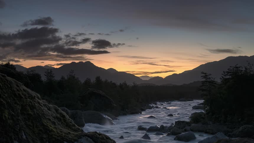 Time lapse of a river flowing in the wilderness near the mountains at sunset