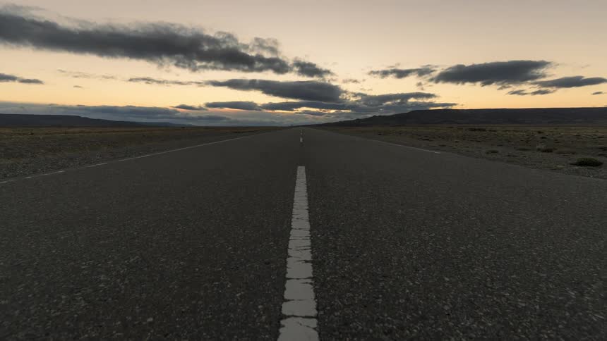 Landscape of a long asphalt road against a reddish sky with the sun setting on the horizon