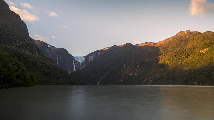 Landscape of a lake surrounded by green mountains and the day getting dark