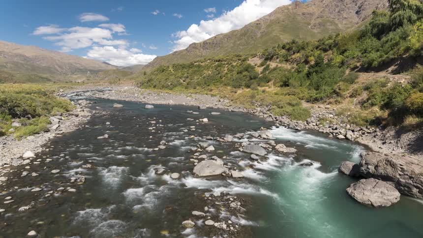 A time lapse of a river shows it flowing through a valley between mountains