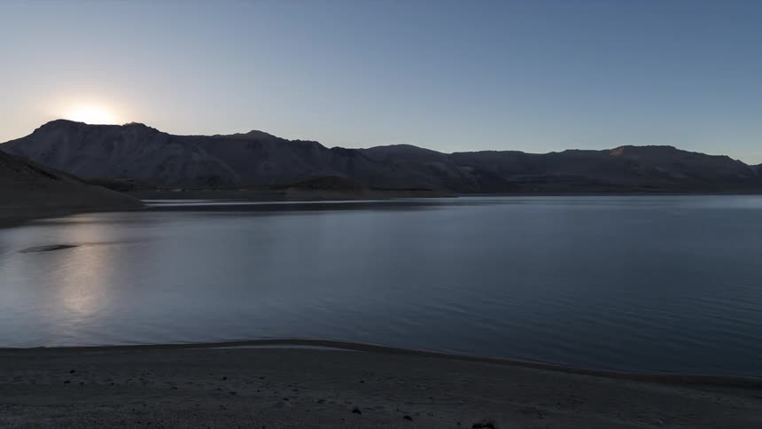 Lake surrounded by mountains with sunrise on the horizon