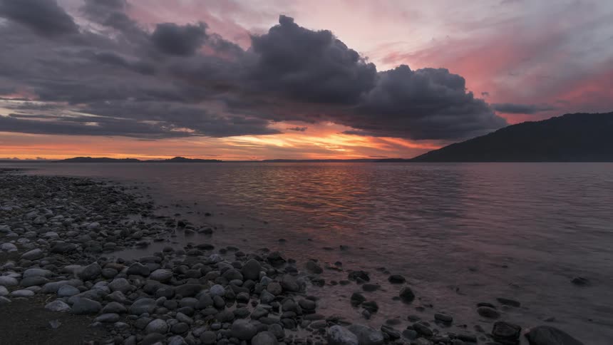 Landscape view of the stormy sky with a sunset on the horizon with the silhouette of mountains on the edge of a lake