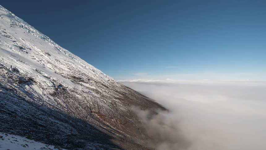 A large mountain is coated in snow and surrounded by a layer of fog