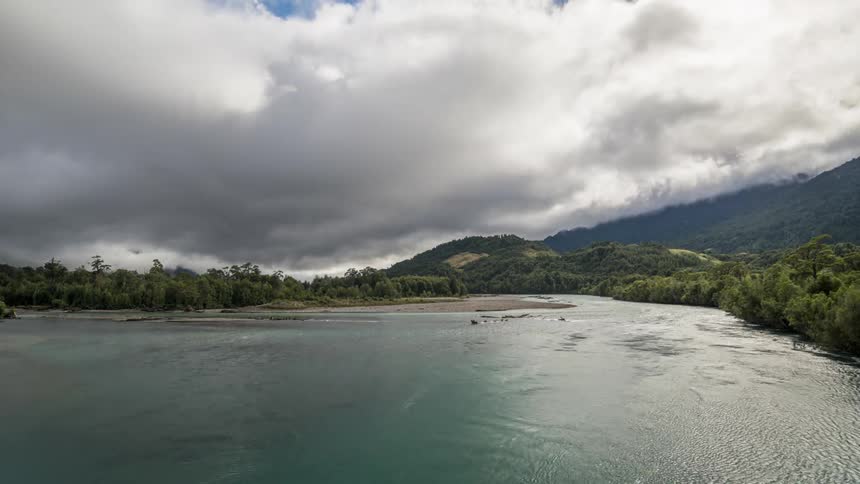 Landscape of a lake surrounded by vegetation in mountains with dense clouds passing by